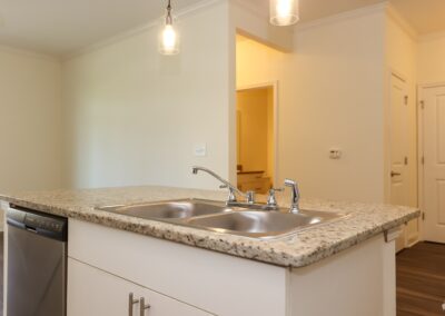 A free-standing kitchen island with a stainless steel double sink set on the white granite countertop and a dishwasher. Two pendant lights hang above the island.