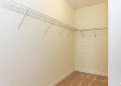 An empty walk-in closet with white wire racks and freshly-vacuumed beige carpet.