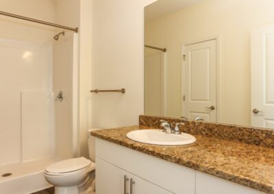 A clean bathroom with a light granite countertop and a shower with an empty curtain rod where a shower curtain can be hung.