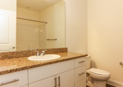 A clean white bathroom with light granite countertops. The mirror reflects a shower with an empty curtain rod where a shower curtain can be hung.